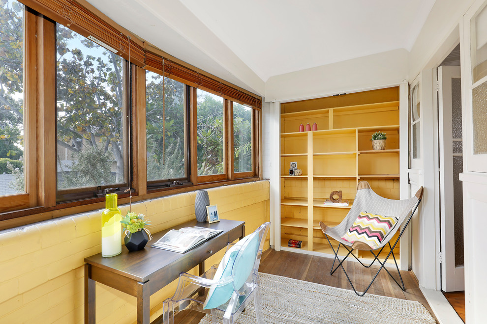 Diseño de despacho vintage de tamaño medio sin chimenea con suelo de contrachapado, suelo marrón, paredes amarillas y escritorio independiente
