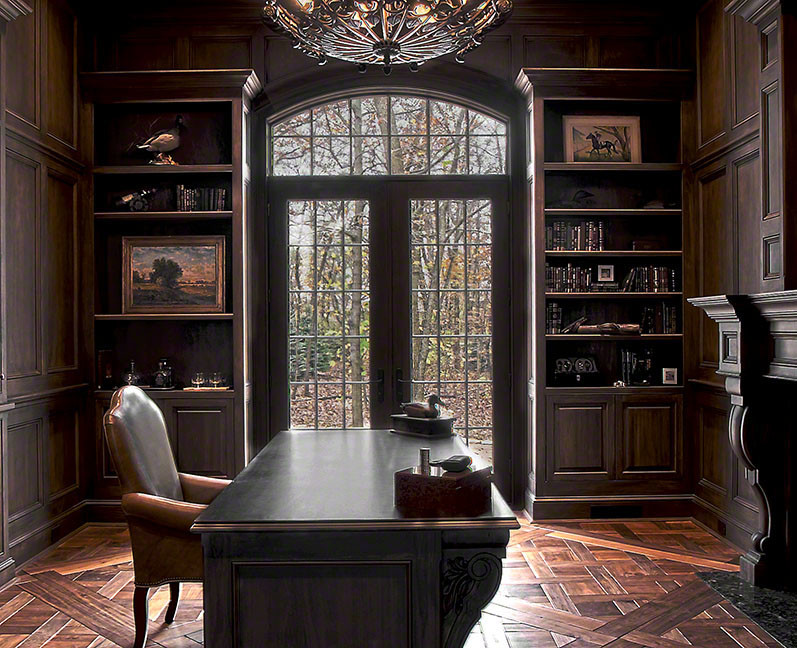 Foto på ett stort rustikt hemmabibliotek, med bruna väggar, mörkt trägolv, en standard öppen spis, en spiselkrans i sten, ett fristående skrivbord och brunt golv
