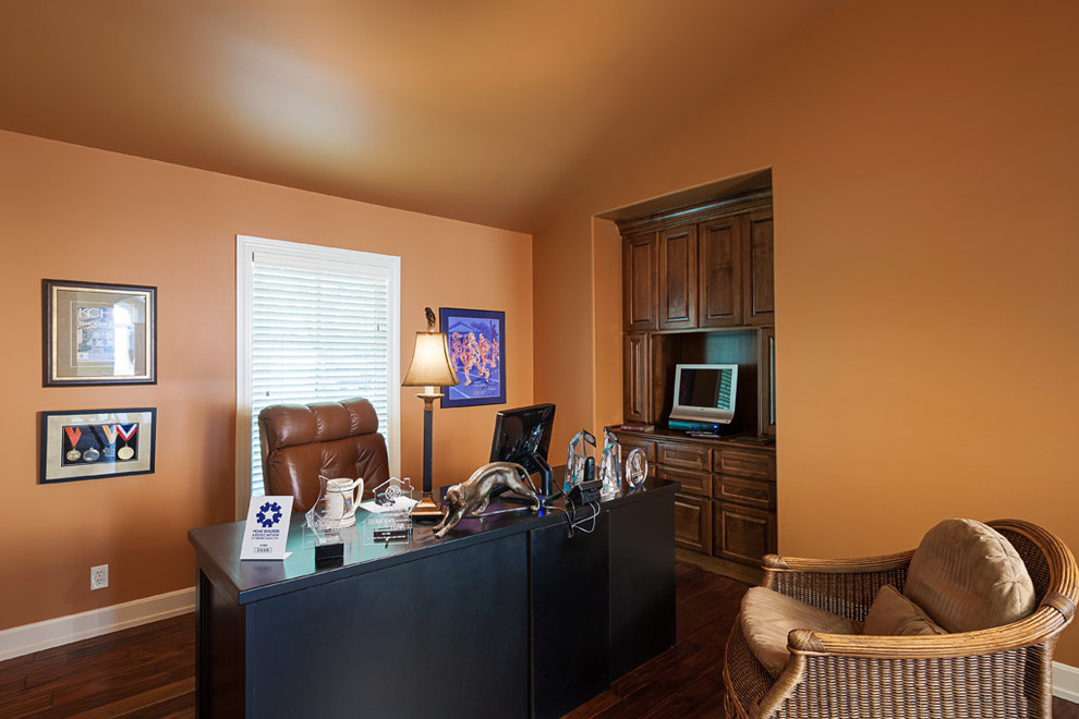 Immagine di un ufficio di medie dimensioni con pareti arancioni, parquet scuro e scrivania autoportante
