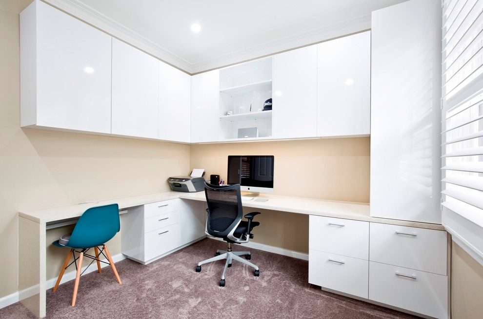 Ejemplo de despacho actual de tamaño medio sin chimenea con paredes beige, moqueta y escritorio empotrado