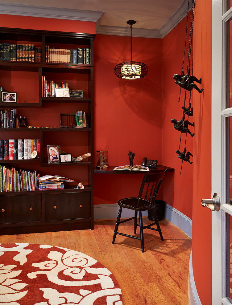 Inspiration för ett mellanstort vintage arbetsrum, med ett bibliotek, röda väggar, mellanmörkt trägolv, ett fristående skrivbord och brunt golv