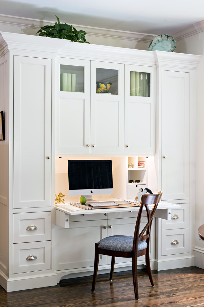 Diseño de despacho tradicional pequeño con paredes blancas, suelo de madera oscura, escritorio empotrado y suelo marrón
