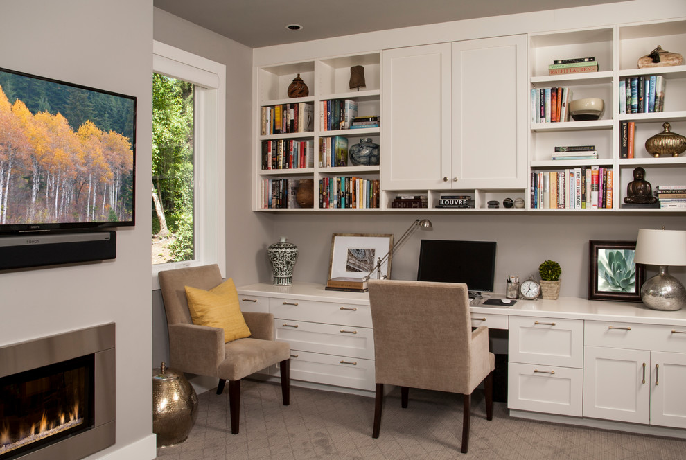 Cette image montre un bureau traditionnel de taille moyenne avec un mur gris, moquette, une cheminée standard, un manteau de cheminée en métal, un bureau intégré et un sol gris.
