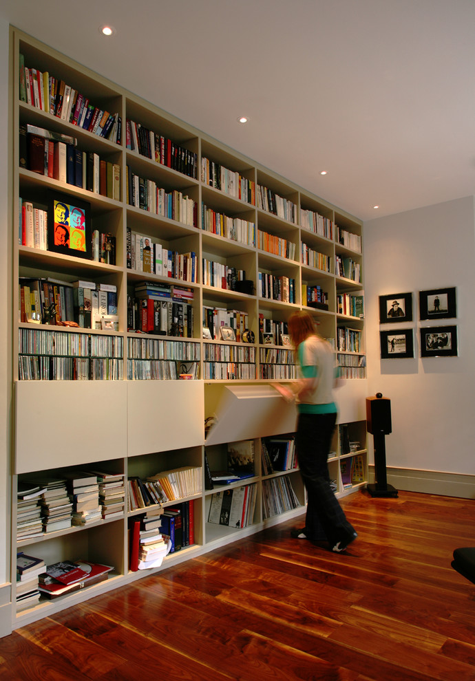 Пример оригинального дизайна: домашняя библиотека в современном стиле с белыми стенами и темным паркетным полом