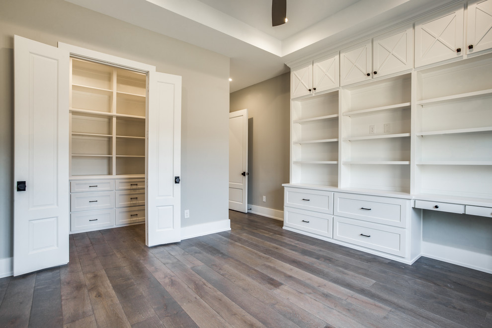Großes Landhausstil Arbeitszimmer ohne Kamin mit grauer Wandfarbe, braunem Holzboden, Einbau-Schreibtisch und braunem Boden in Dallas
