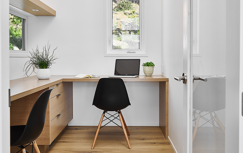 Modelo de despacho minimalista pequeño con paredes blancas, suelo de madera clara y escritorio empotrado