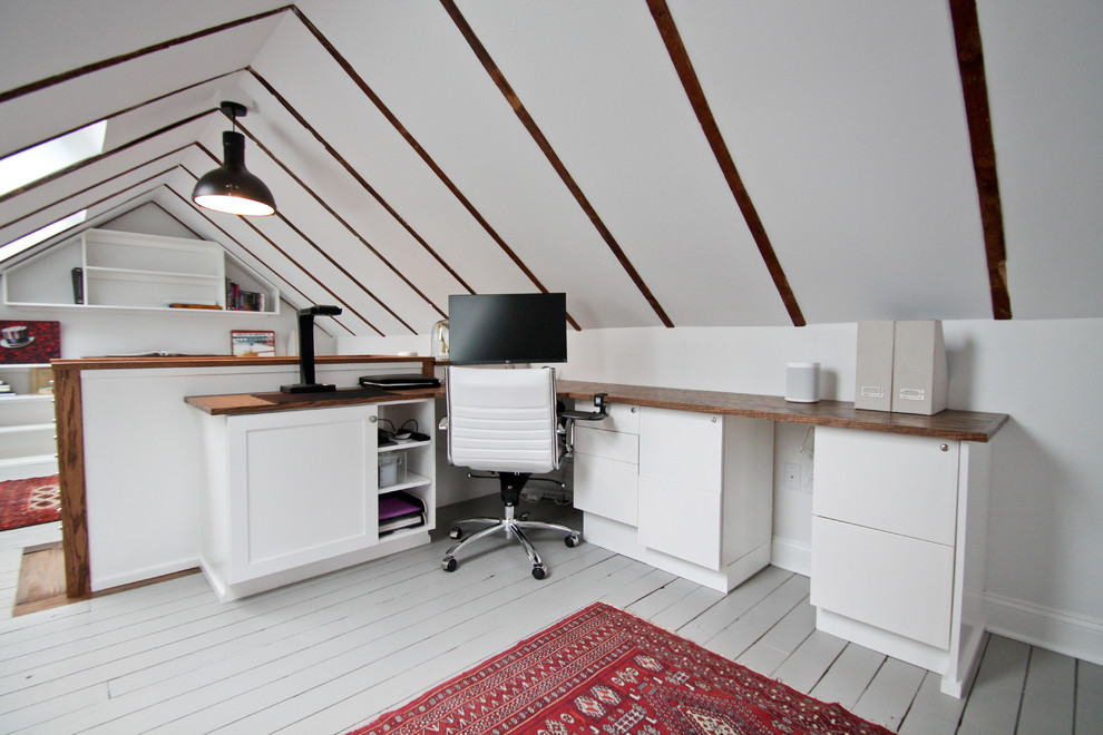 Foto på ett mellanstort lantligt hemmabibliotek, med vita väggar, målat trägolv, ett inbyggt skrivbord och grått golv