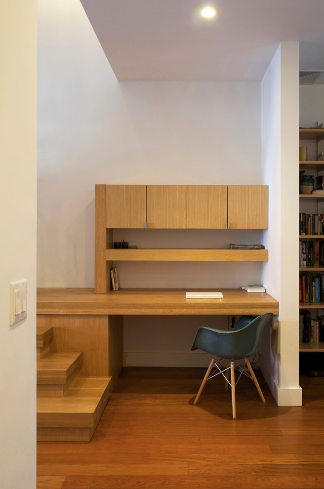 Foto på ett mellanstort funkis hemmabibliotek, med ett inbyggt skrivbord, vita väggar och ljust trägolv