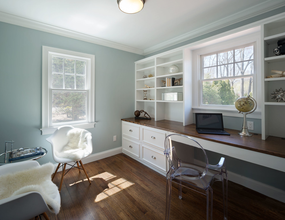 This is an example of a small traditional study in New York with blue walls, dark hardwood flooring and a built-in desk.