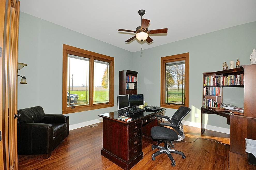 Klassisches Arbeitszimmer ohne Kamin mit grüner Wandfarbe, braunem Holzboden und freistehendem Schreibtisch in Indianapolis
