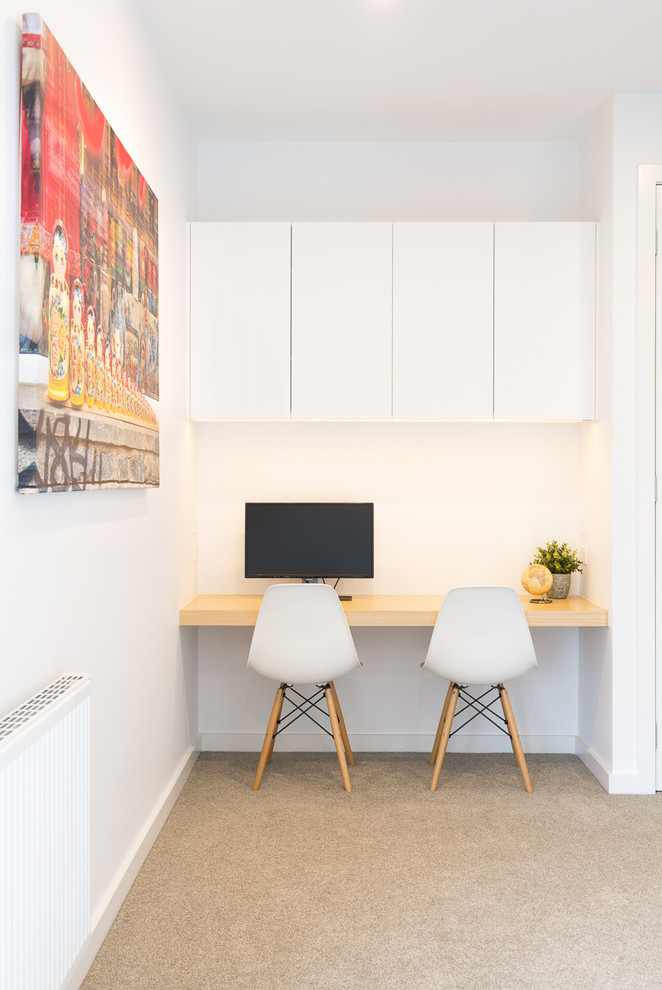 Immagine di un piccolo ufficio design con pareti bianche, moquette, scrivania incassata e pavimento beige