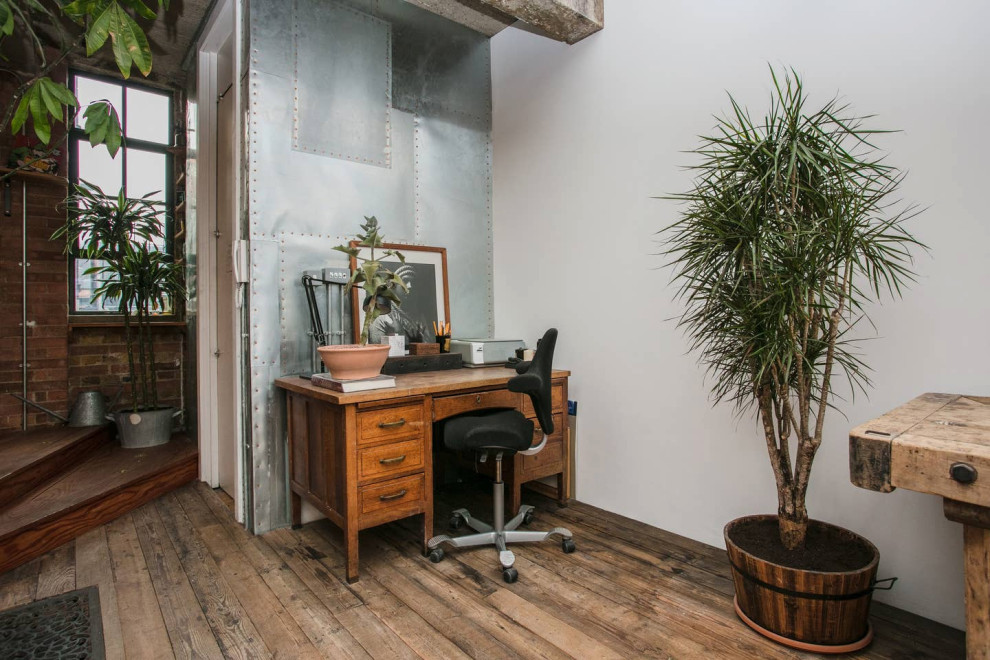 Idee per uno studio industriale con pareti bianche, pavimento in legno massello medio, scrivania autoportante e pavimento marrone