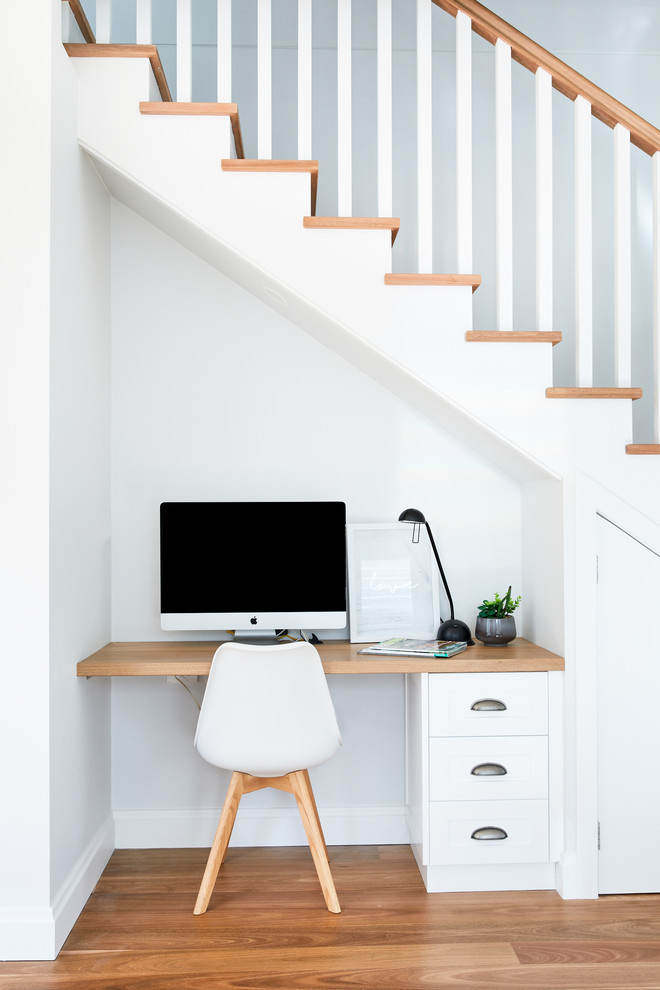 Idee per un piccolo ufficio stile marinaro con pareti bianche, scrivania incassata, parquet chiaro e nessun camino