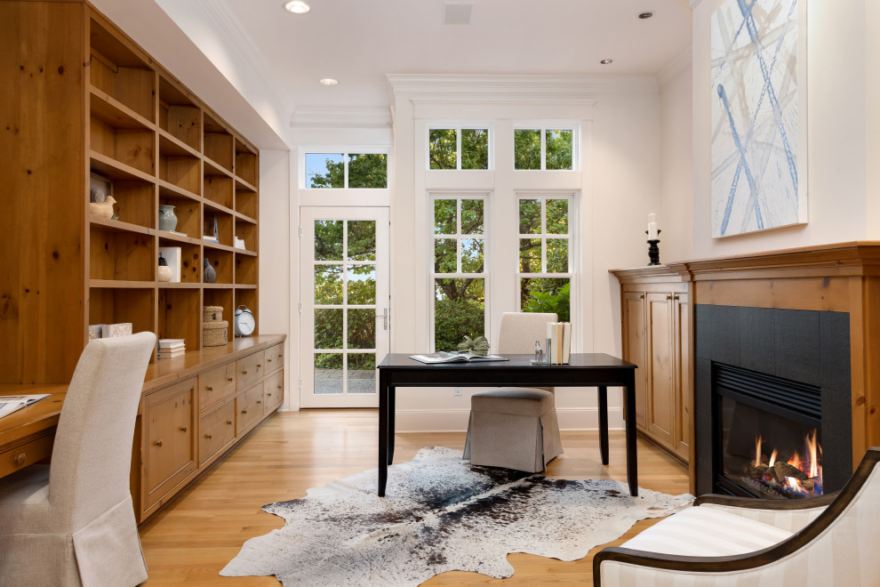 シアトルにある広いトラディショナルスタイルのおしゃれな書斎 (白い壁、無垢フローリング、標準型暖炉、木材の暖炉まわり、自立型机、茶色い床) の写真