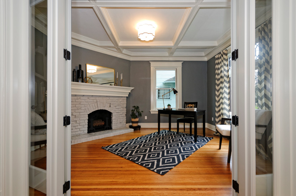 Cette image montre un bureau traditionnel de taille moyenne avec un mur gris, un sol en bois brun, une cheminée standard, un manteau de cheminée en brique et un bureau indépendant.