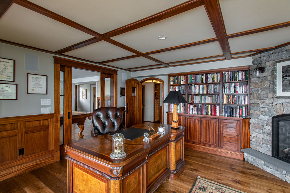 Großes Klassisches Lesezimmer mit grauer Wandfarbe, braunem Holzboden, Kamin, Kaminumrandung aus Stein, Einbau-Schreibtisch und braunem Boden in Boston
