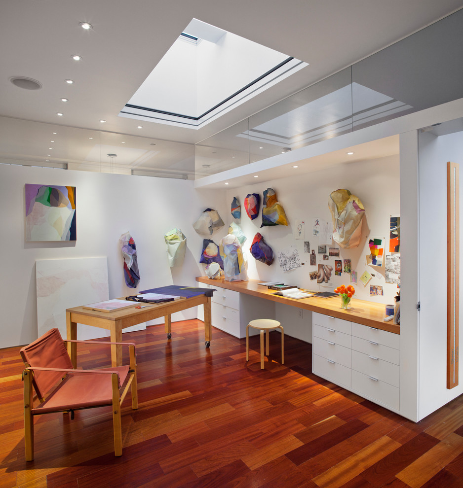 Modernes Arbeitszimmer ohne Kamin mit Studio, weißer Wandfarbe, braunem Holzboden und Einbau-Schreibtisch in New York