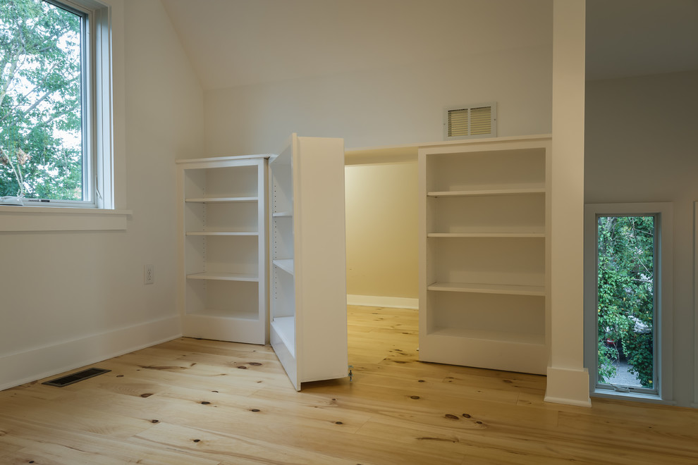 Ejemplo de estudio actual grande con paredes blancas, suelo de madera clara y escritorio independiente