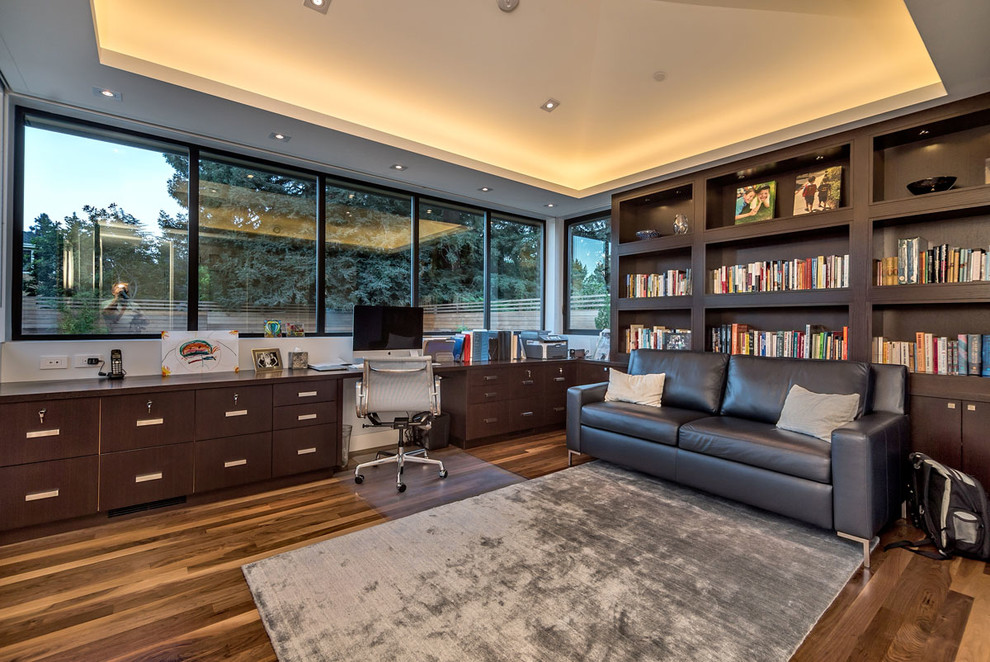 Cette image montre un grand bureau design avec un mur gris, un sol en bois brun et un bureau intégré.