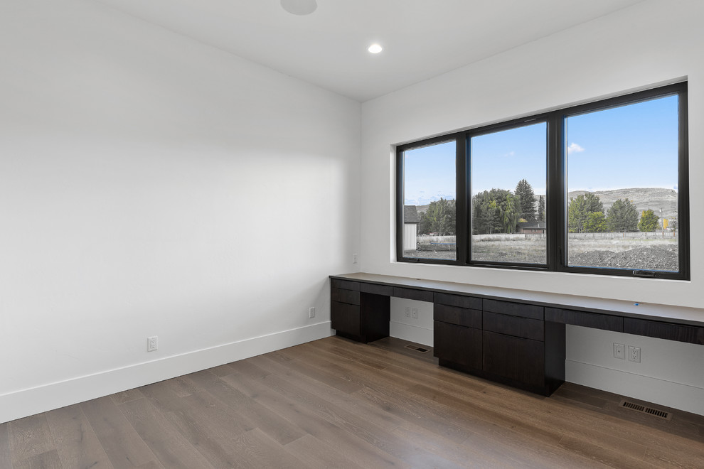 Ejemplo de despacho actual extra grande sin chimenea con paredes blancas, suelo de madera en tonos medios, escritorio empotrado y suelo marrón