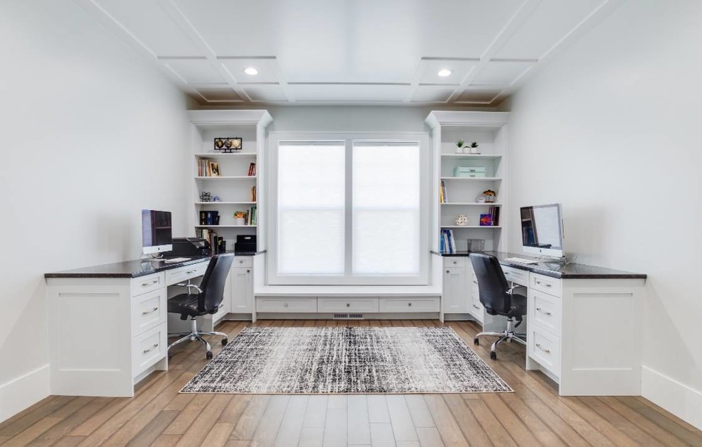 Modelo de despacho clásico renovado de tamaño medio sin chimenea con paredes blancas, suelo de madera clara, escritorio empotrado y suelo beige