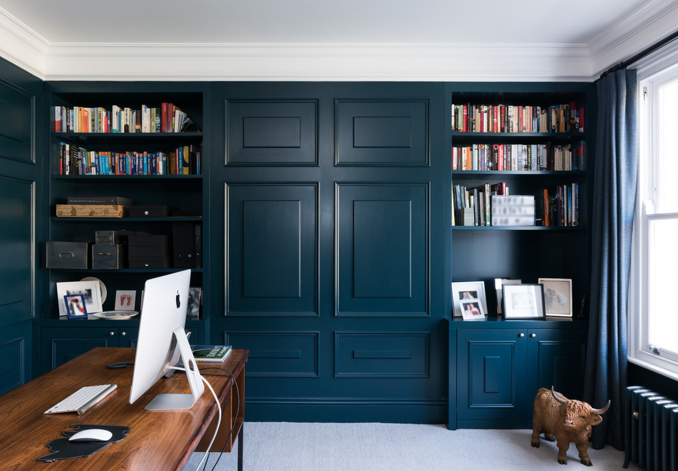 Klassisk inredning av ett mellanstort hemmabibliotek, med blå väggar, heltäckningsmatta, ett fristående skrivbord och beiget golv