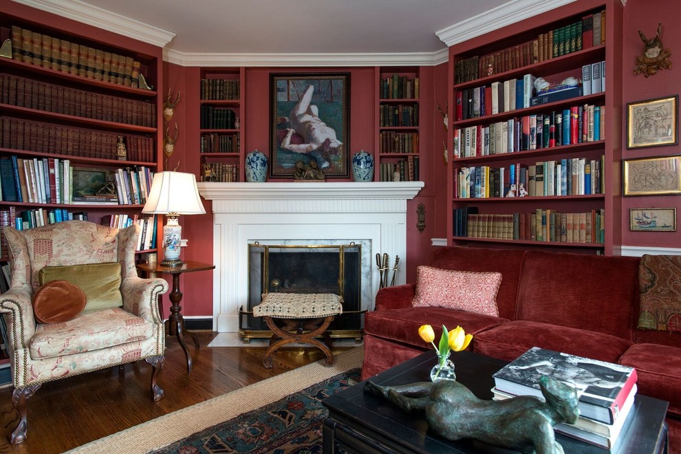 Foto på ett vintage arbetsrum, med ett bibliotek, röda väggar, mellanmörkt trägolv, en standard öppen spis, en spiselkrans i trä och brunt golv