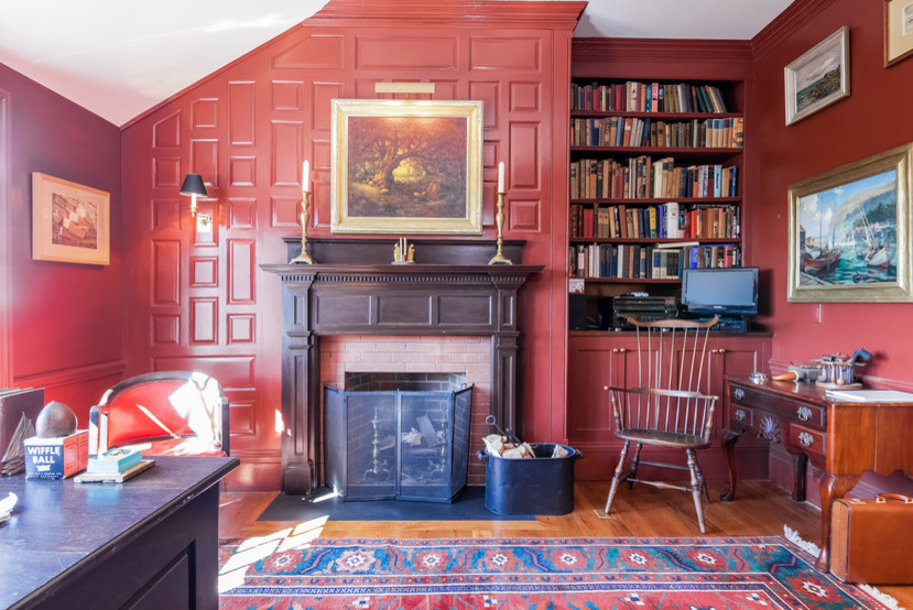 Bild på ett mellanstort vintage hobbyrum, med röda väggar, ljust trägolv, en standard öppen spis, ett fristående skrivbord och en spiselkrans i tegelsten