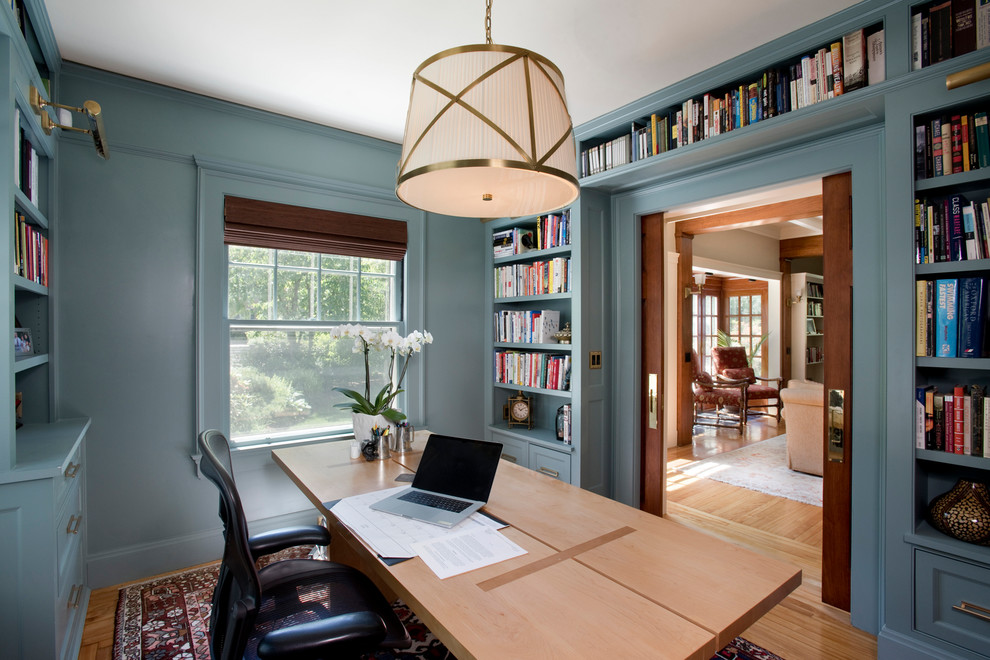 Exempel på ett amerikanskt hemmabibliotek, med blå väggar, ljust trägolv och ett fristående skrivbord