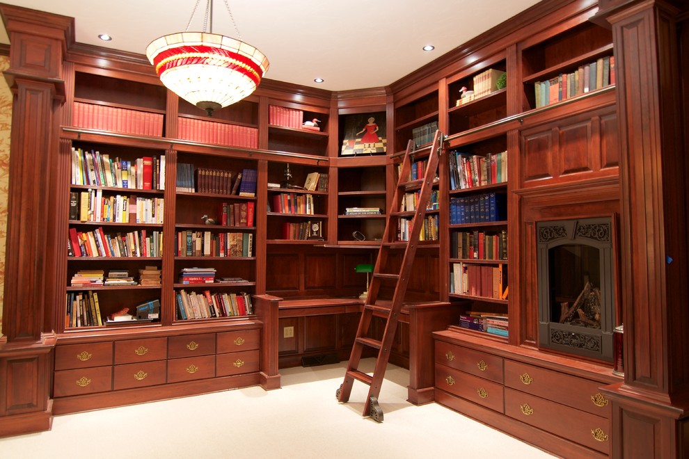 Inspiration för stora klassiska hemmabibliotek, med heltäckningsmatta, en standard öppen spis, en spiselkrans i metall, ett inbyggt skrivbord och bruna väggar