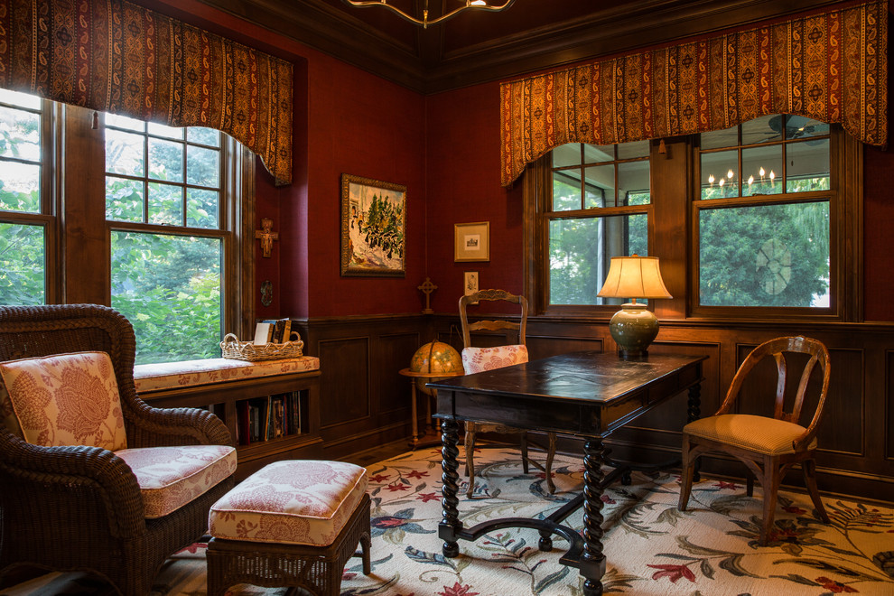 Inspiration för stora klassiska hemmabibliotek, med röda väggar, mörkt trägolv, ett fristående skrivbord och brunt golv