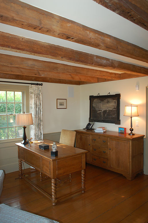 Maritim inredning av ett mellanstort hemmabibliotek, med vita väggar, mellanmörkt trägolv och ett fristående skrivbord