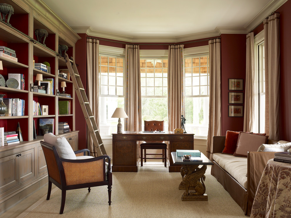 Imagen de despacho de estilo de casa de campo grande sin chimenea con biblioteca, paredes rojas, suelo de madera clara, escritorio independiente y suelo beige