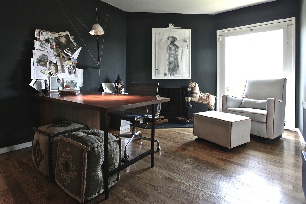 Eklektisk inredning av ett litet arbetsrum, med svarta väggar, mörkt trägolv, ett fristående skrivbord och en öppen hörnspis