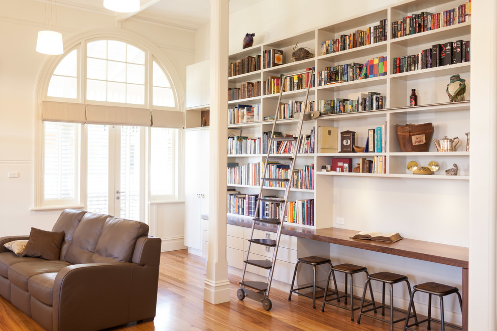 Idéer för mellanstora funkis hemmabibliotek, med vita väggar, mellanmörkt trägolv och ett inbyggt skrivbord