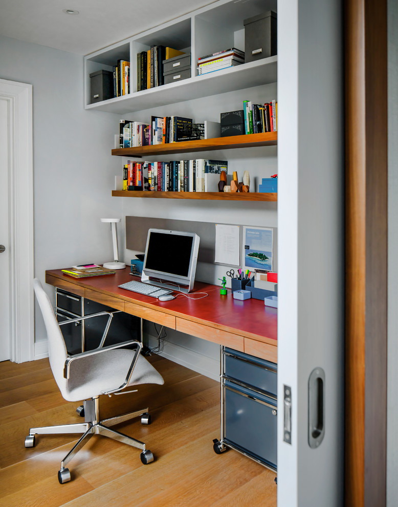Modern inredning av ett arbetsrum, med grå väggar, mellanmörkt trägolv och ett inbyggt skrivbord