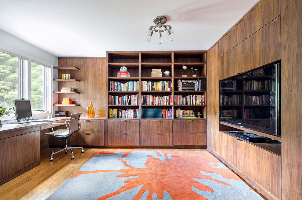 Inredning av ett modernt stort hemmabibliotek, med bruna väggar, ljust trägolv och ett inbyggt skrivbord