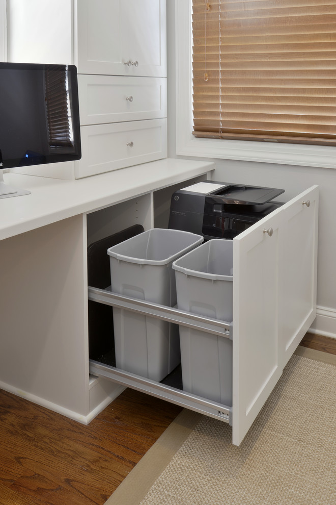 Cette image montre un grand bureau design avec un mur blanc, un sol en bois brun et un bureau intégré.