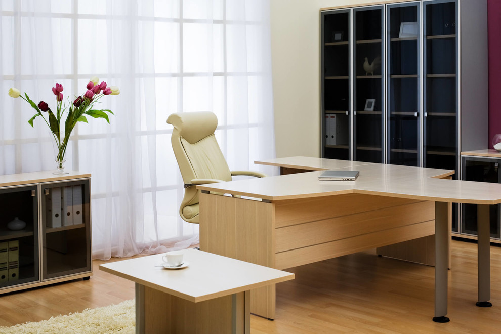 Diseño de despacho actual de tamaño medio con paredes beige, suelo de madera clara, escritorio independiente y suelo beige