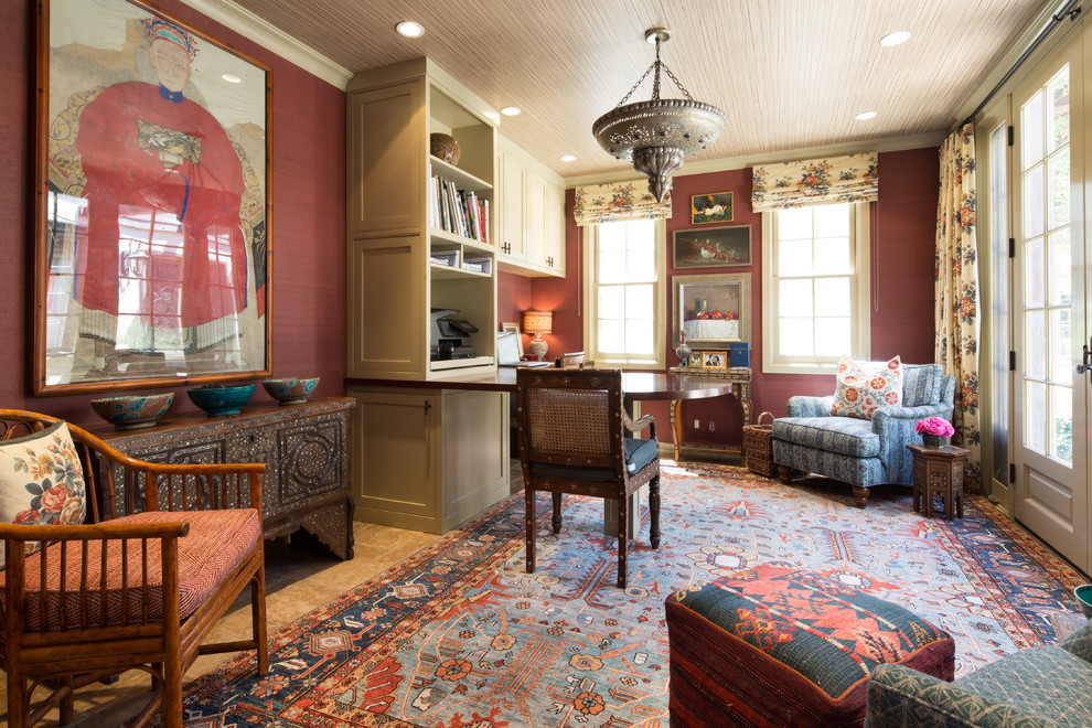 Eklektisk inredning av ett mellanstort hemmabibliotek, med röda väggar, travertin golv och ett inbyggt skrivbord