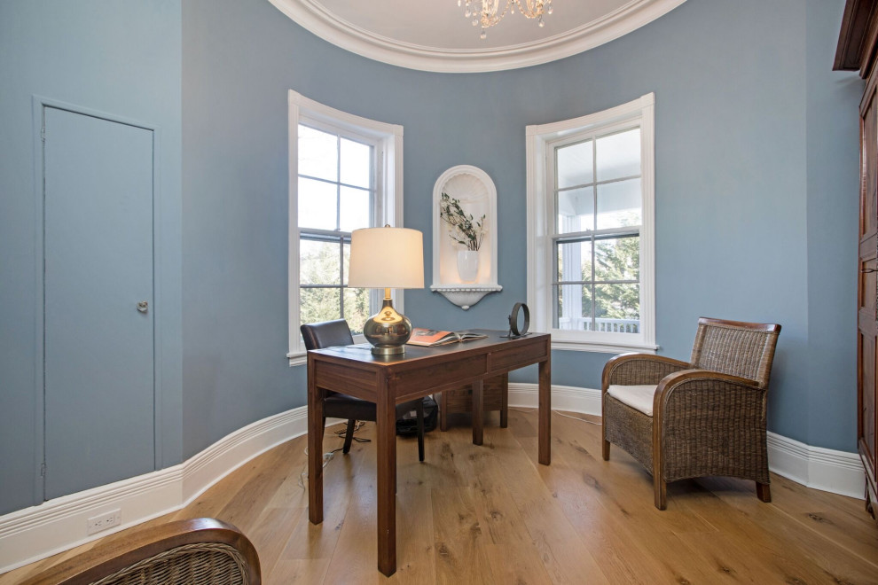 Photo of a traditional study in New York with blue walls, medium hardwood flooring, a freestanding desk and brown floors.