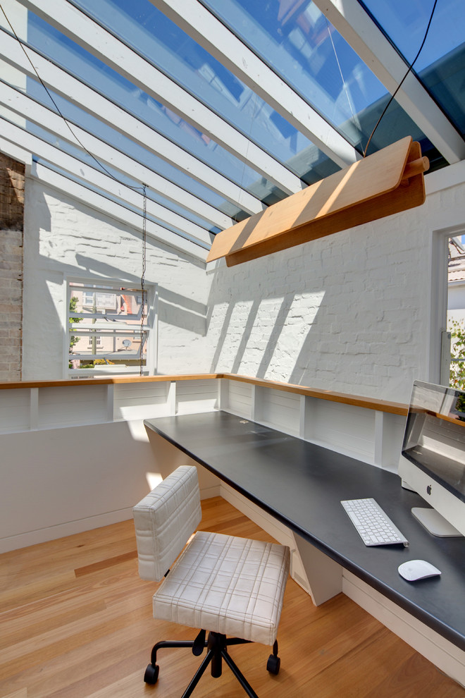 Diseño de estudio minimalista pequeño con paredes blancas, suelo de madera clara y escritorio empotrado