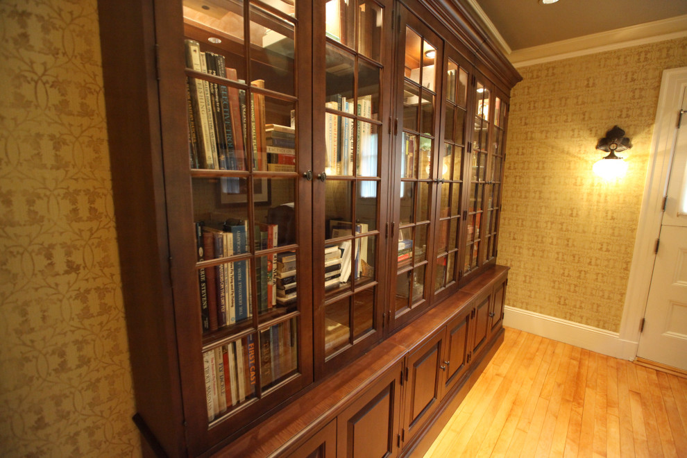 Diseño de despacho beige tradicional de tamaño medio con biblioteca, paredes beige, suelo de madera en tonos medios, escritorio independiente y suelo marrón