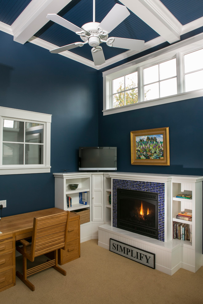 Foto på ett mellanstort amerikanskt hemmabibliotek, med blå väggar, heltäckningsmatta, en standard öppen spis, en spiselkrans i trä, ett fristående skrivbord och beiget golv