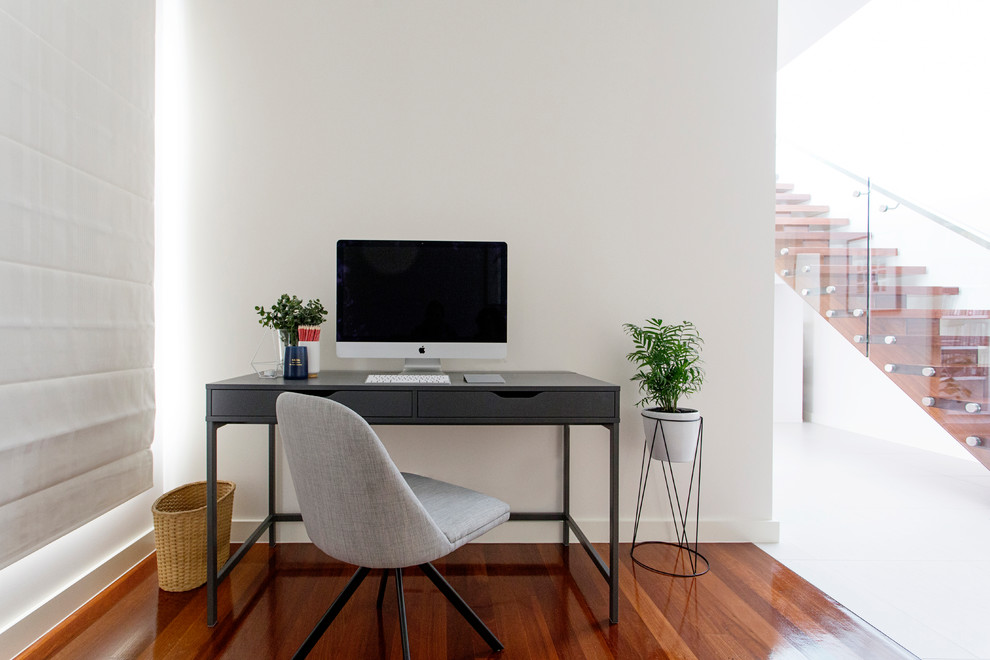 Exempel på ett litet modernt arbetsrum, med vita väggar, mellanmörkt trägolv, en standard öppen spis och en spiselkrans i gips