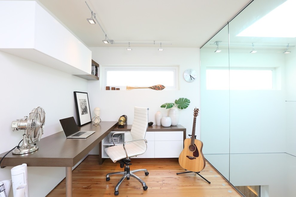 Modelo de despacho contemporáneo de tamaño medio sin chimenea con paredes blancas, suelo de madera clara y escritorio empotrado