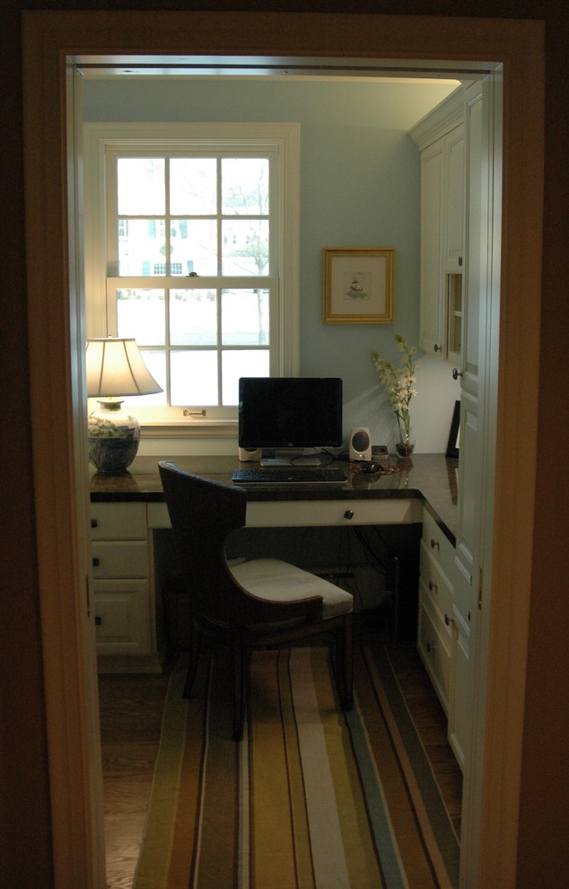 Klassisk inredning av ett litet hemmabibliotek, med blå väggar, mellanmörkt trägolv och ett inbyggt skrivbord