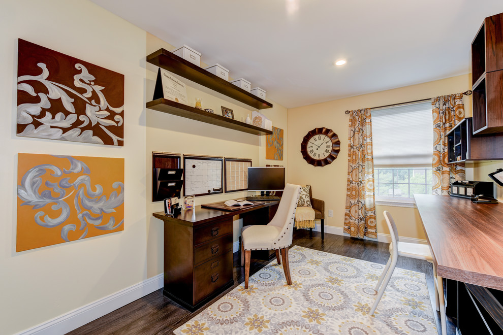 Kleines Klassisches Arbeitszimmer ohne Kamin mit gelber Wandfarbe, dunklem Holzboden und freistehendem Schreibtisch in Philadelphia
