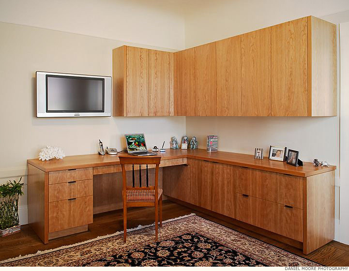Foto på ett stort hemmabibliotek, med vita väggar, mellanmörkt trägolv och ett inbyggt skrivbord
