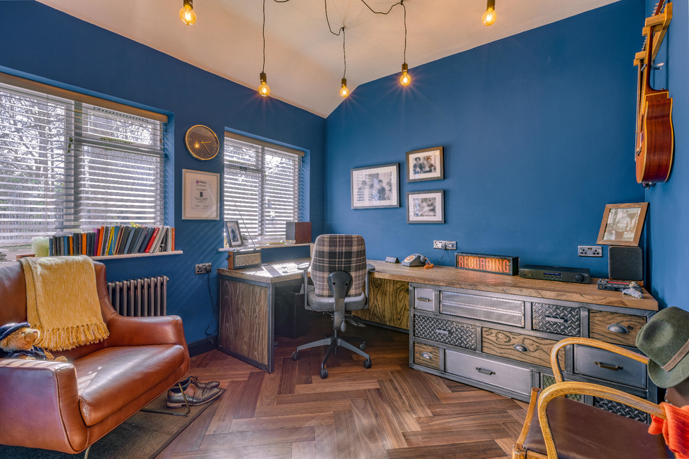 Ejemplo de despacho industrial con paredes azules, suelo de madera oscura, escritorio empotrado y suelo marrón